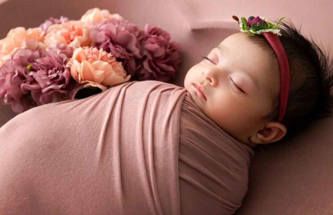 Wrapped in dreams! Baby girl in a soft brown swaddle with floral accents in a baby photography session.